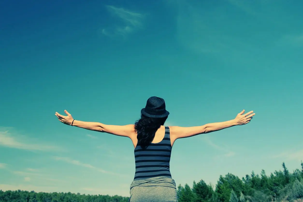 Person outdoors with arms outstretched in nature.