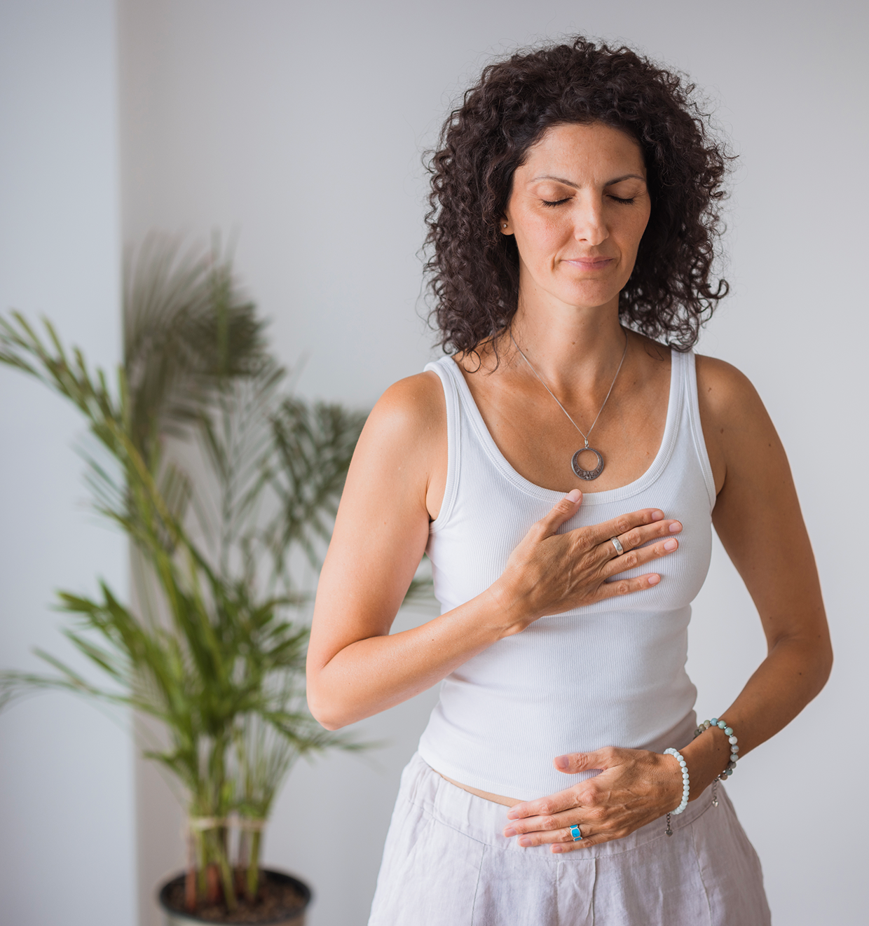 Woman meditating with eyes closed, indoor plant.