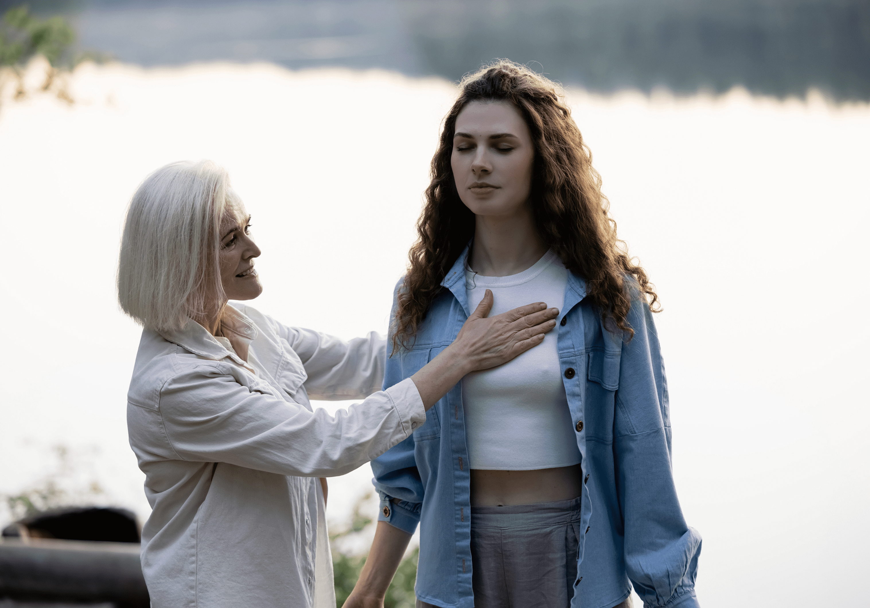 Woman guiding another in meditation outdoors.
