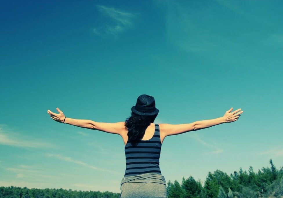 Person outdoors with arms outstretched in nature.